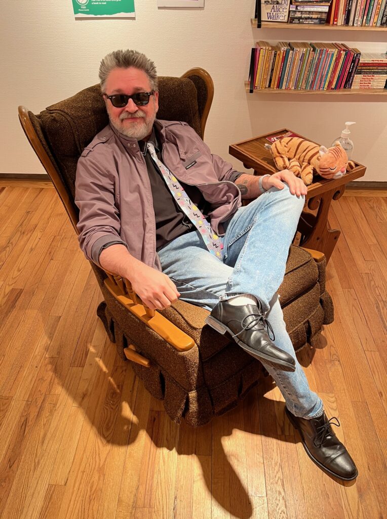 Pat Green in 80s Sunglasses, members only vintage jacket, and acid washed jeans. The chair is vintage too.