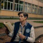 A young man reading a book and holding a coffee cup on a college campus in Serbia.
