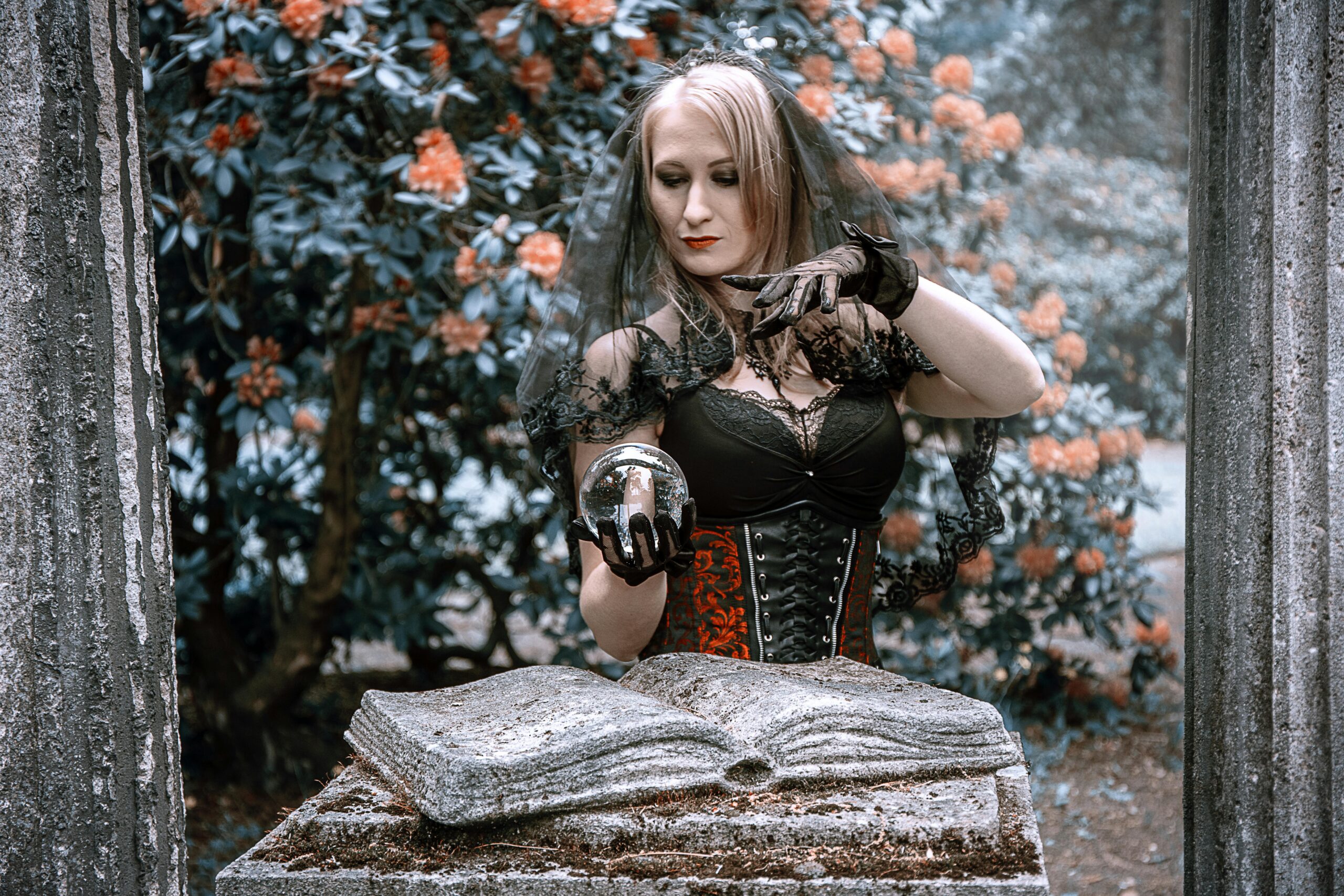 A woman dressed as a witch holds a crystal ball in a mysterious outdoor setting.